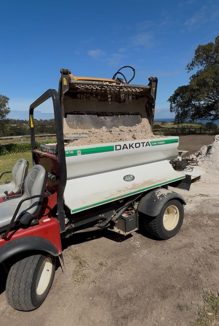 Loader bucket filling a vehicle-mounted Dakota topdresser with sand