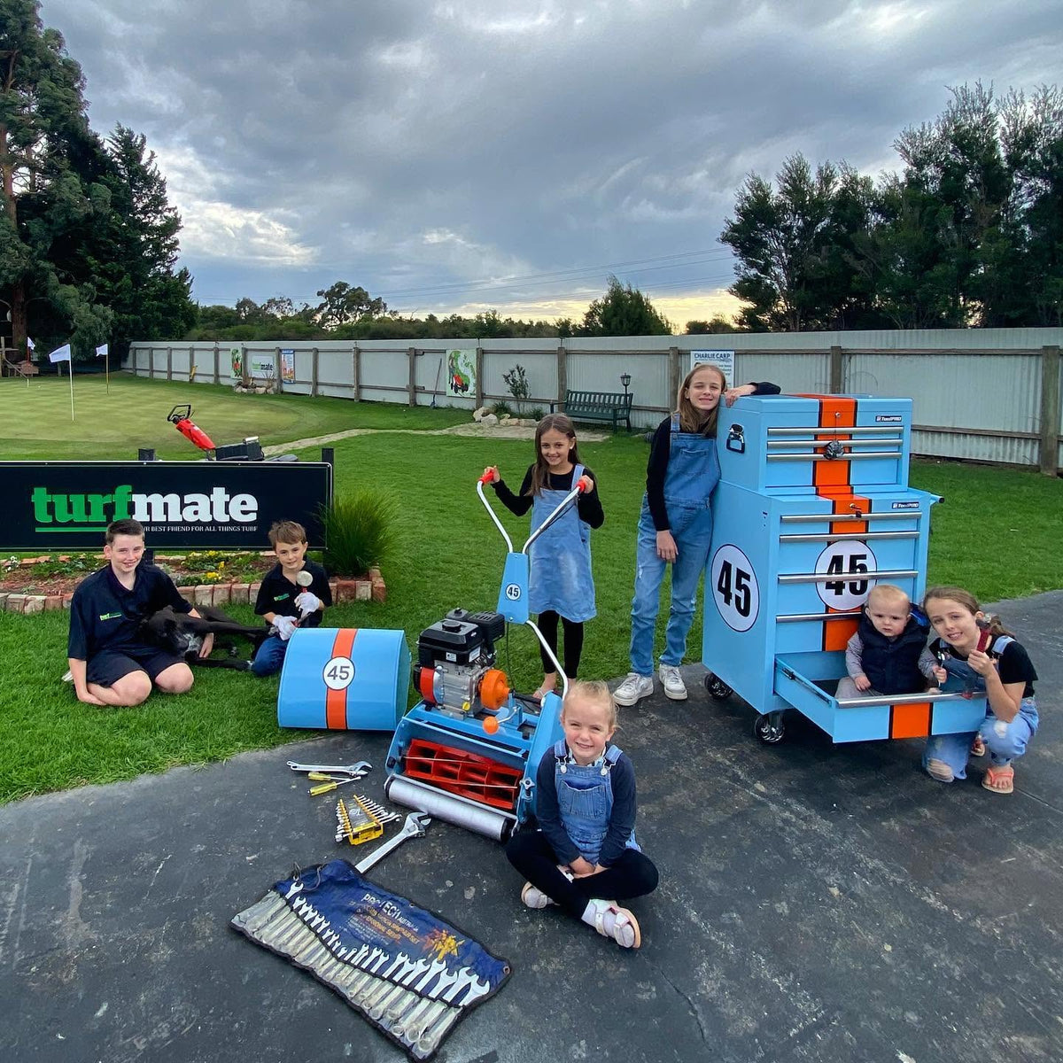 The Turfmate family with a mower and tools beside the Turfmate sign.